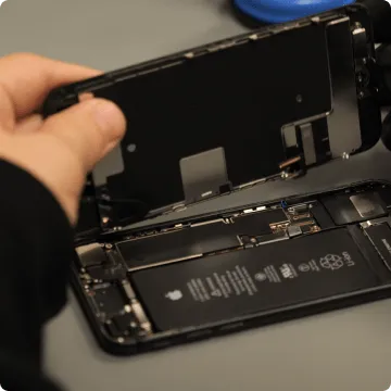 Ein hinten geöffnetes Smartphone. Daumen und Zeigefinger klappen die Hinterseite nach oben, darunter ist der Akku des gebrauchten Handys zu sehen.