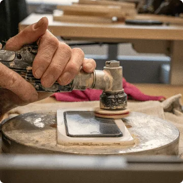 Das refurbished Smartphone liegt eingeklemmt in einer weißen Vorrichtung. Zwei Hände polieren das iPhone mit einer speziellen Bürste.